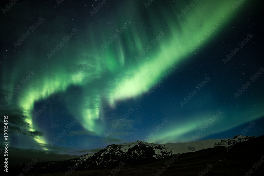 Northern lights aka Aurora Borealis glowing on the sky with mountains in Iceland