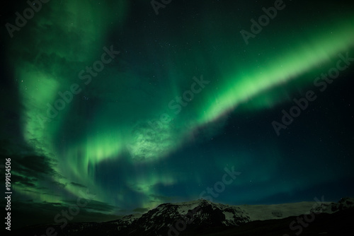 Northern lights aka Aurora Borealis glowing on the sky with mountains in Iceland © Jamo Images