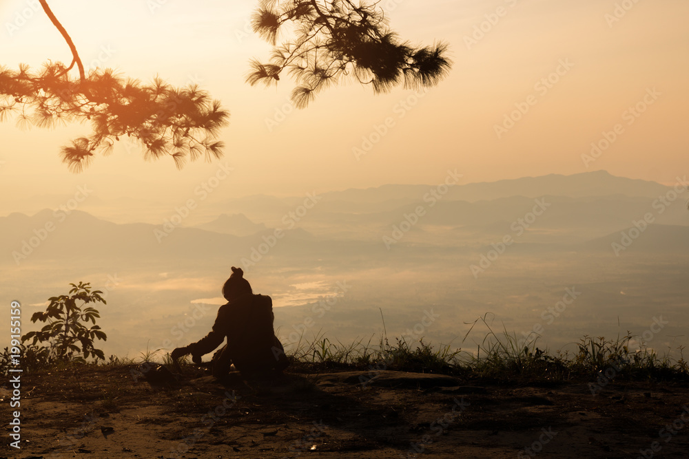 Woman sitting serenely of the cliff and looking at the valley and mountains in the morning