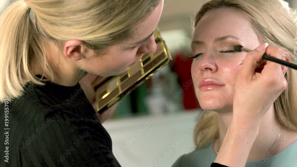 Professional makeup artist applying classic eye makeup to blonde woman. Perfect eyeshadow look. Best smokey eye look. Professional makeup artist applying classic eye makeup to blonde woman. Perfect eyeshadow look. Best smokey eye look.
