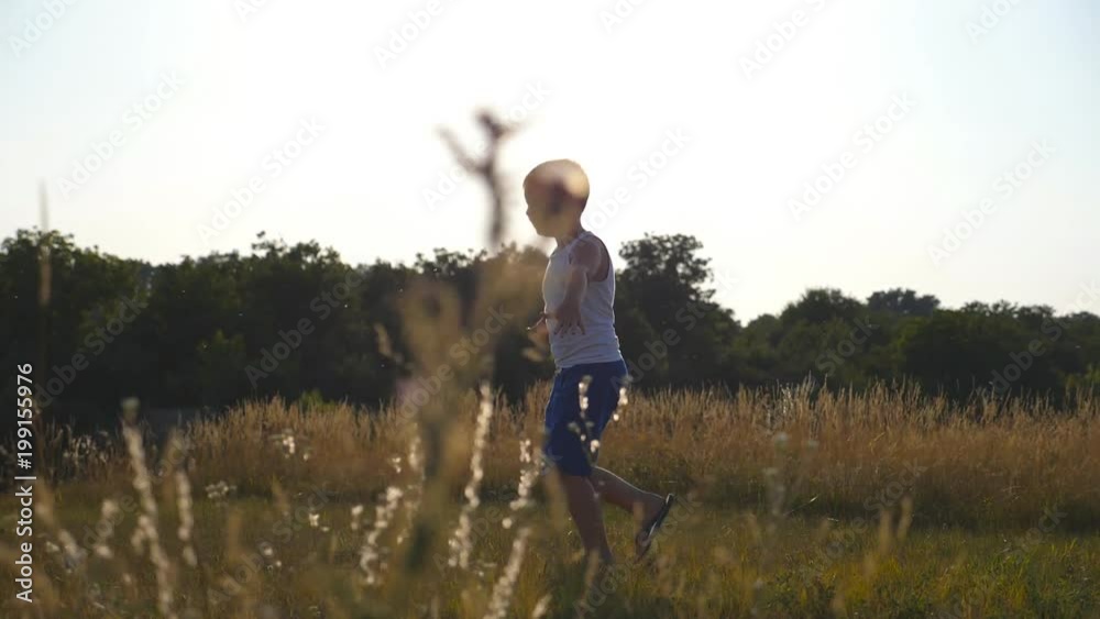Young boy with raised hands running on green grass at the field on sunny day. Child jogging at the lawn outdoor. Happy smiling male kid having fun in nature on a summer meadow. Slow motion Close up Young boy with raised hands running on green grass at the field on sunny day. Child jogging at the lawn outdoor. Happy smiling male kid having fun in nature on a summer meadow. Slow motion Close up