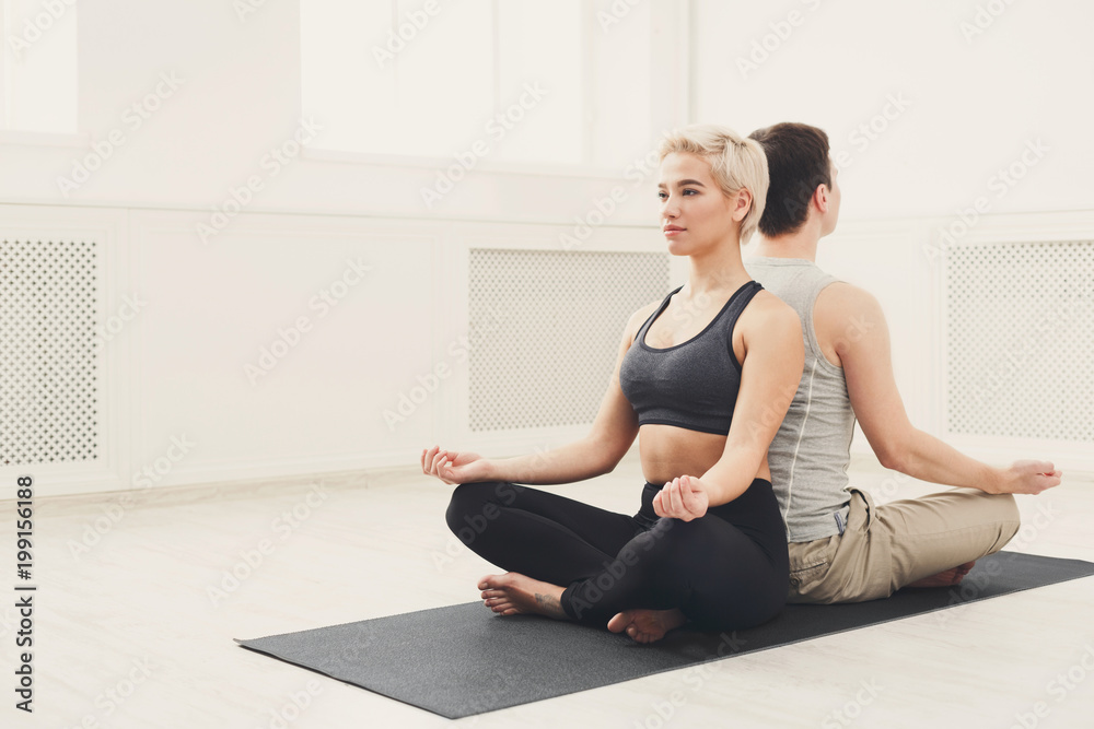 Young couple meditating together, back to back Young couple meditating together, back to back