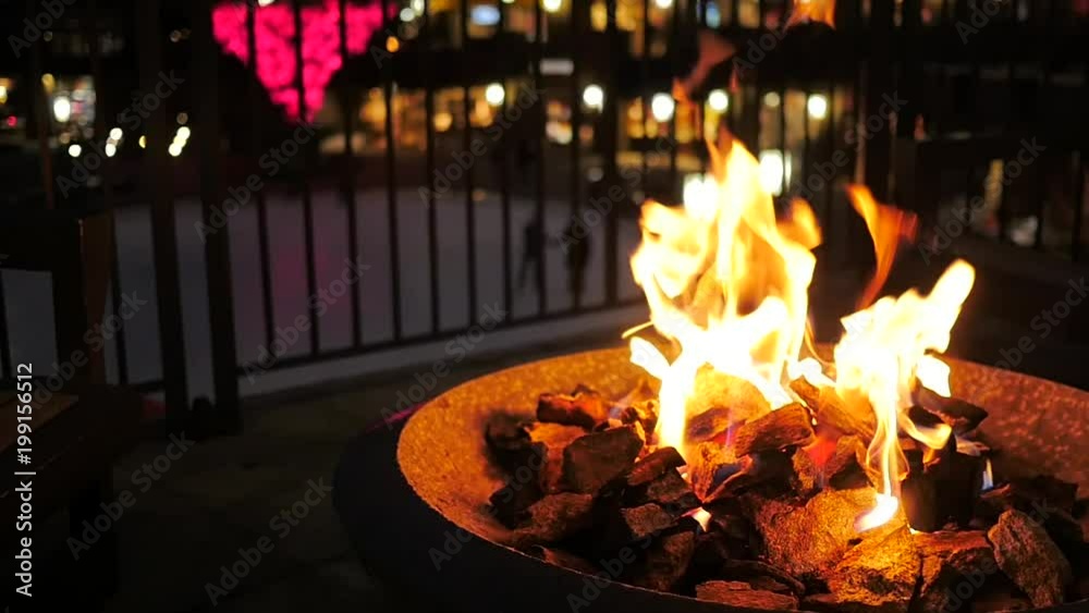 Slow motion outdoor fire pit in the winter with ice skaters in the background