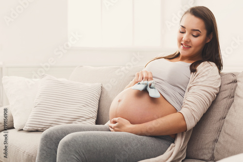 Pregnant woman holding tiny shoes near belly