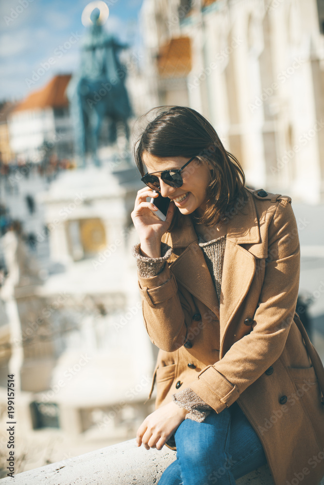Fototapeta premium Trendy young woman sitting outdoor and using mobile phone