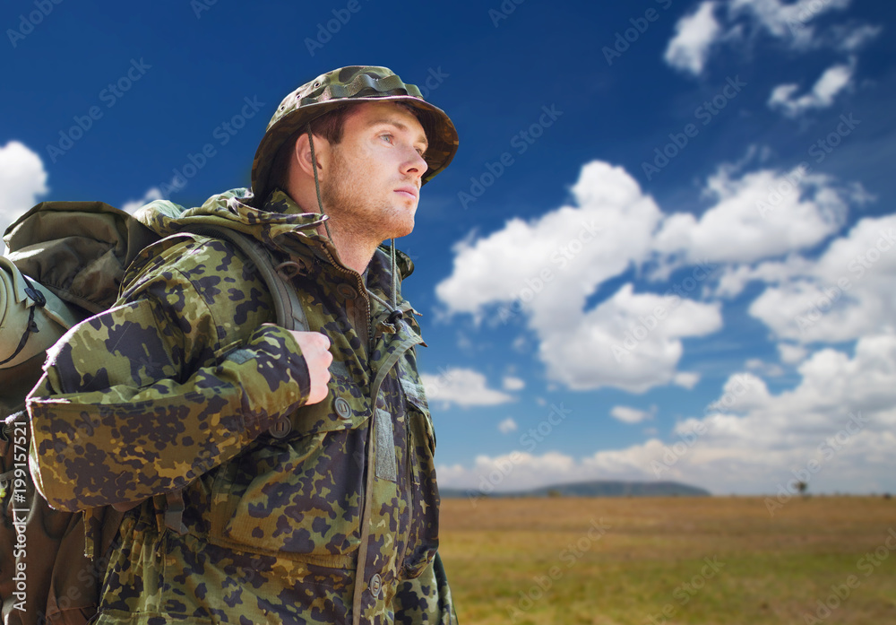 army, military service, travel and tourism concept - young soldier or traveler in camouflage uniform with backpack hiking over natural background and blue sky