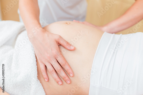 Close to the female hands of a massage therapist makes a light massage to the belly of a pregnant girl in a cosmetology room