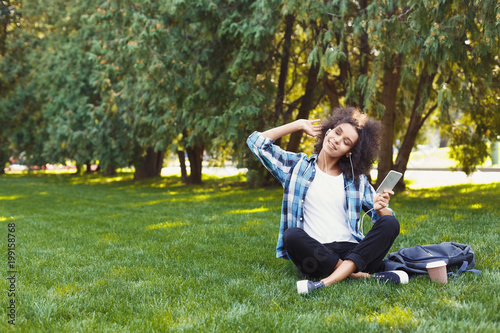 Young woman listening to music on grass outdoors © Prostock-studio