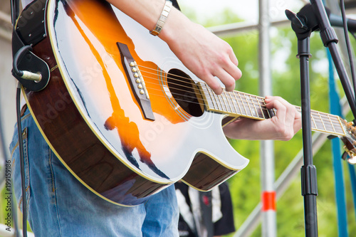 Musical band perfom on an open air festival. Guitarist man playing music by wooden acoustic guitar close-up photo