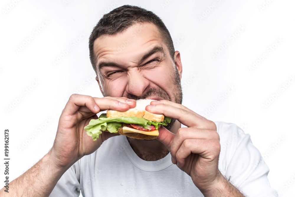 Funny and hungry guy is eating some fast food. He is hungry like a wolf.  Man is biting sandwich very hard. Isolated on white background. Stock Photo  | Adobe Stock