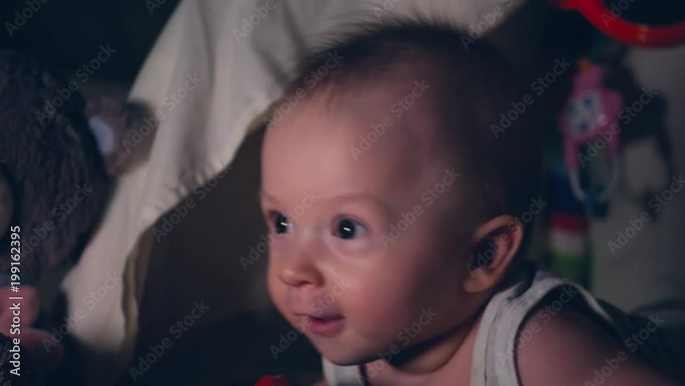 Little baby boy plays at night under a blanket by the light of a small lamp Little baby boy plays at night under a blanket by the light of a small lamp
