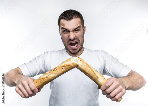 Emotional picture of strong guy breaking a baguette in the middle of it. The bread is fresh but nit very healthy. This freak guy likes to do this kind of stuff. Isolated on white background. photo