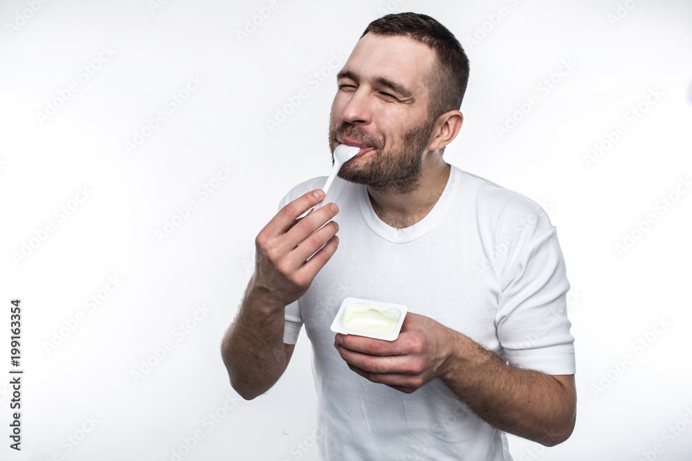 Young and strong man is eating yogurt. He is doing that with pleasure. Isolated on white background. Young and strong man is eating yogurt. He is doing that with pleasure. Isolated on white background.