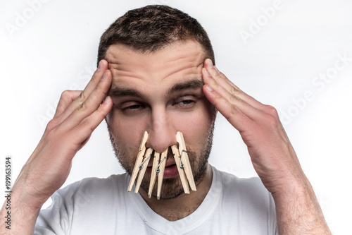 Man has a headache and his nose is running. He has an allergy. He is suffering from that. Man's nose is closed with clothpins. Isolated on white background. photo