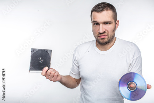 Young man holding a compact disk in one hand and a box from it in another hand and staring at camera. Time goes so fast that now he doesn't know what to do with this disk. Isolated on white background photo