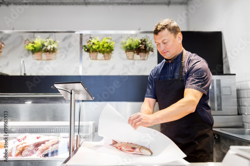 Fotografía food sale, small business and people concept - male seller wrapping fresh fish i