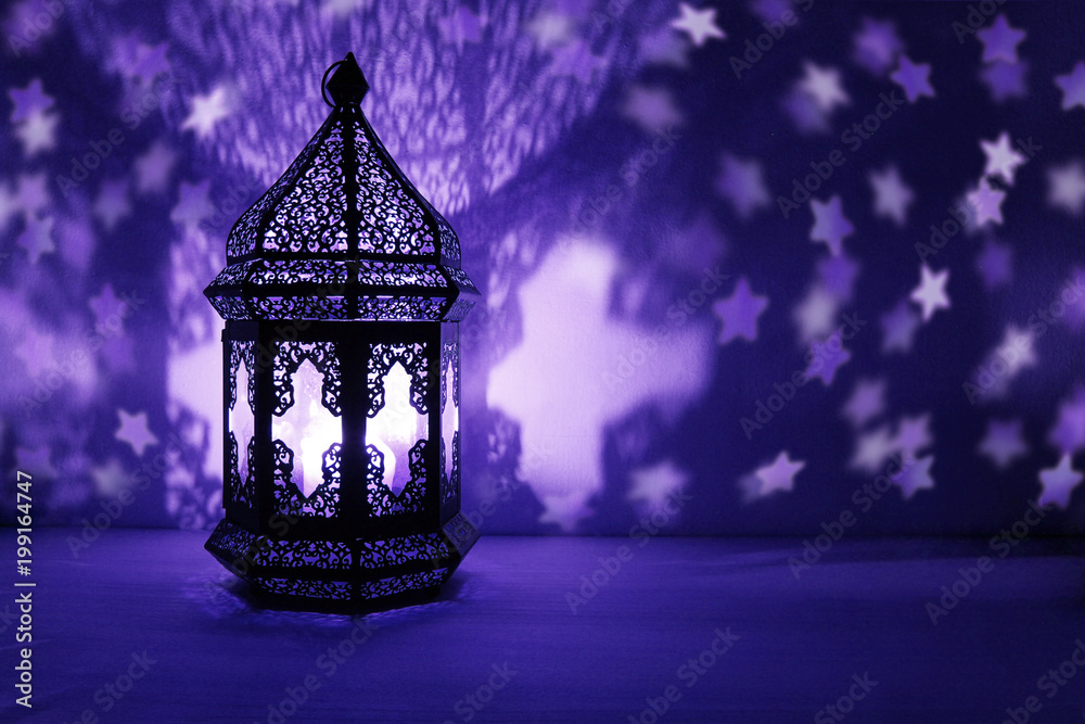 Ornamental Arabic lantern with burning candle glowing at night and glittering stars shaped bokeh lights. Festive greeting card, invitation for Muslim holy month Ramadan Kareem. Dark background.