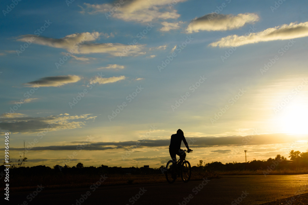 Image of cyclist rides bicycle on sunset time background. A man rides a bike on the road with beautiful colorful sky. Sport and active life concept.