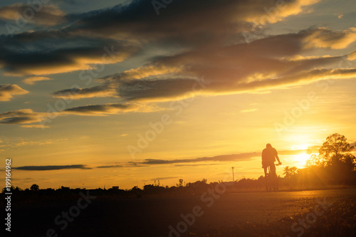 Image of cyclist rides bicycle on sunset time background. A man rides a bike on the road with beautiful colorful sky. Sport and active life concept.