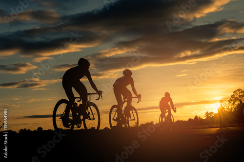 The men ride  bikes at sunset with orange-blue sky background. Abstract Silhouette background concept. © Pattadis
