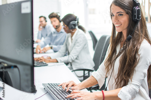 Beautiful smiling customer support agent operator woman with headset working on desktop computer in call center