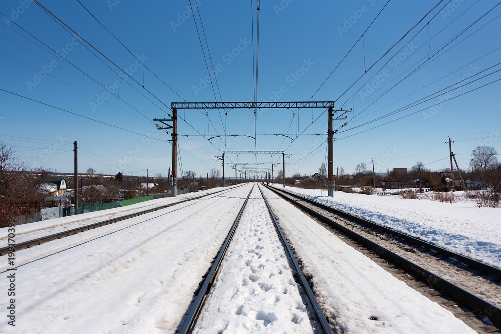 Railway in winter. Railroad tracks far beyond the city. Snow-covered winter landscape on a sunny day.