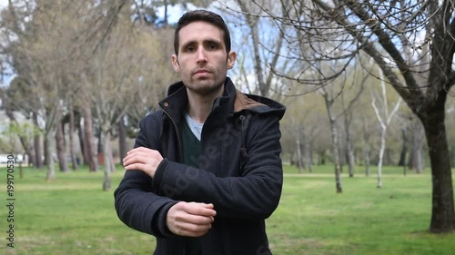 Hombre joven dirigiéndose a cámara mientras pasea por el campo, se cruza de brazos y mira serio.