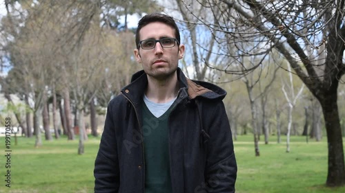 Hombre joven serio mira a cámara y se pone unas gafas