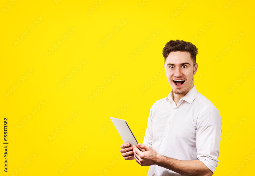 Surprised young man wearing white shirt using tablet pc Surprised young man wearing white shirt using tablet pc