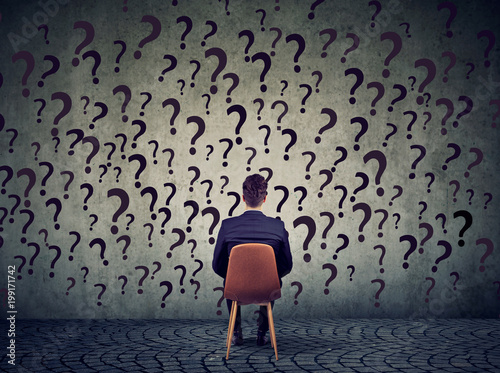 business man sitting on a chair in front of a wall has many questions, wondering what to do next photo