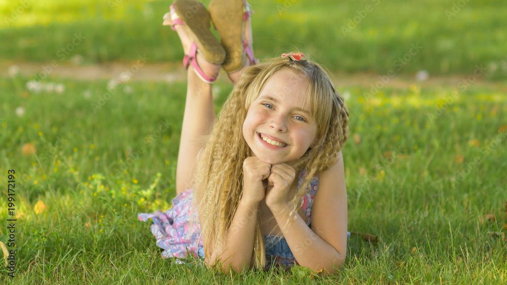 Beautiful young blonde girl lying on a field, green grass. Outdoors Enjoy Nature. Healthy Smiling Girl lying in Green Grass Beautiful young blonde girl lying on a field, green grass. Outdoors Enjoy Nature. Healthy Smiling Girl lying in Green Grass