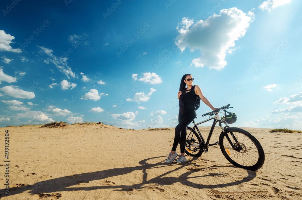 Bicyclist the summer sunset on the desert road in the reserve territory. Full length image of young female cyclist. Summer sunset. Bicycle and ecology lifestyle concept.