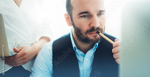 Bearded young businessman working on modern office. Consultant man thinking looking in monitor computer. Manager coworking on workplace, discussio startup project concept in studio with colleague photo