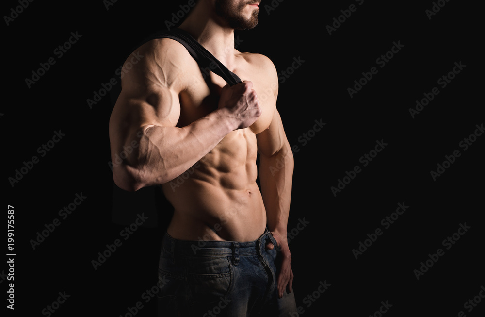 Portrait of shirtless muscular man in a jeans. Young male hunk showing his perfect body and muscles on black background.