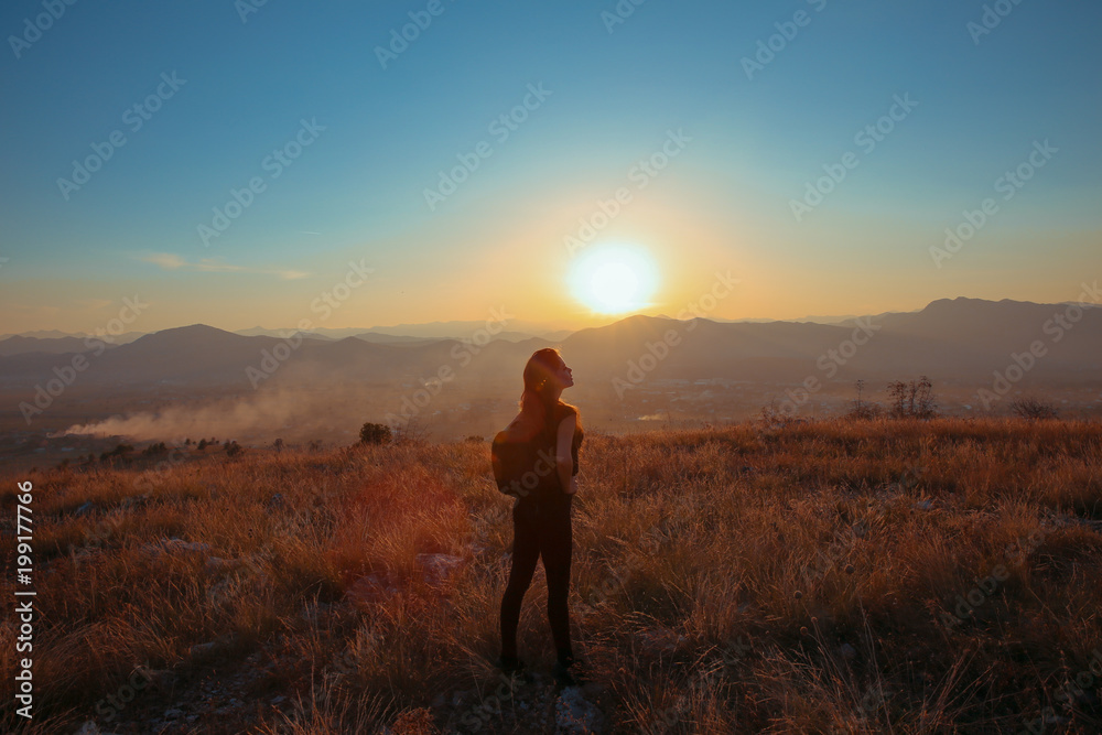 Sunset mountain. Tourist Free happy  woman outstretched arms with backpack enjoying life in wheat field. Hiker cheering elated and blissful with arms raised.