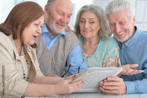 two senior couples reading newspaper