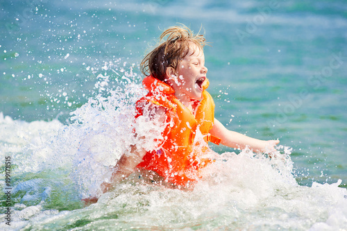 Little boy in orange life vest swimming in wave sea (selective DOF)