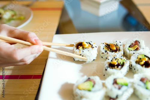 Woman's hand picking up sushi with chopsticks.