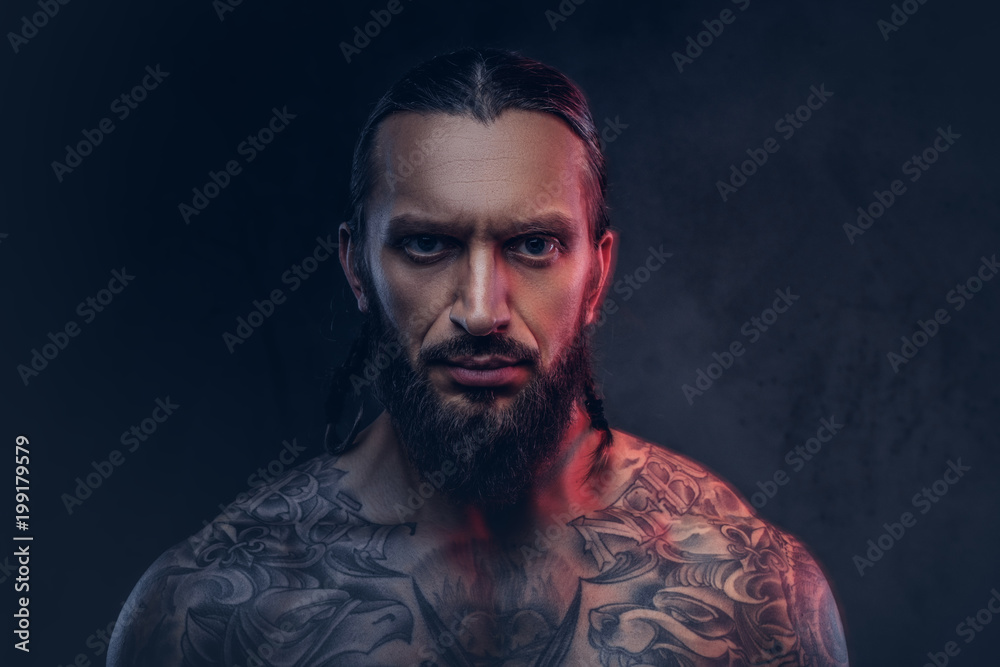 Close-up portrait of a muscular bearded tattoed male with a stylish haircut, isolated on a dark background. Close-up portrait of a muscular bearded tattoed male with a stylish haircut, isolated on a dark background.