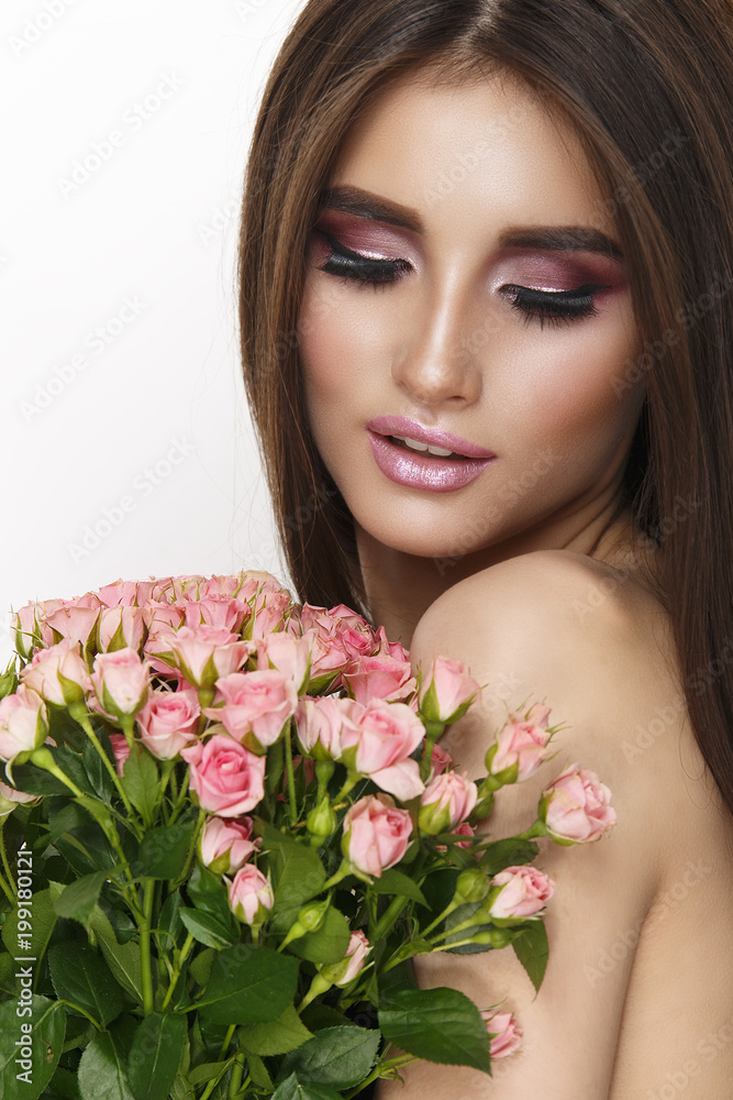 Beautiful sexy girl with green eyes, gentle makeup and pink lips. Lovely girl with a bouquet of pink roses looking at flowers.