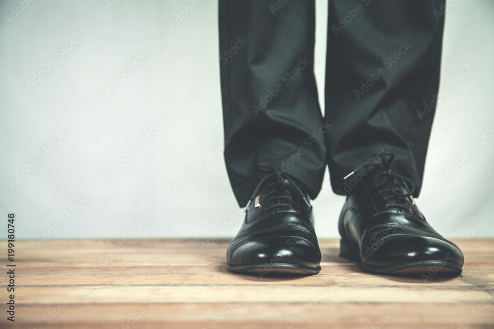 Man feet in black leather shoes stands on wooden floor.