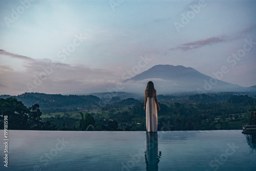 beautiful girl staying near swimming pool with fantastic volcano Agung view