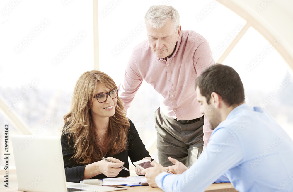 Close-up ofmiddle aged businesswoman consulting with senior manager and young assistant while sitting at office desk and working together on new project. Teamwork. Close-up ofmiddle aged businesswoman consulting with senior manager and young assistant while sitting at office desk and working together on new project. Teamwork.