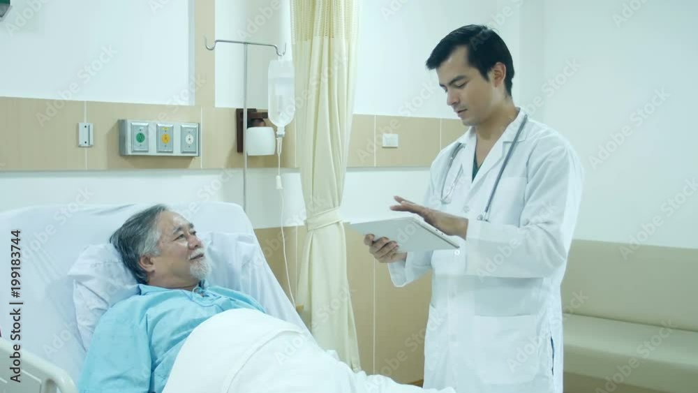 Old patient lying in hospital bed. Doctor holding tablet and taking to him. Old patient lying in hospital bed. Doctor holding tablet and taking to him.