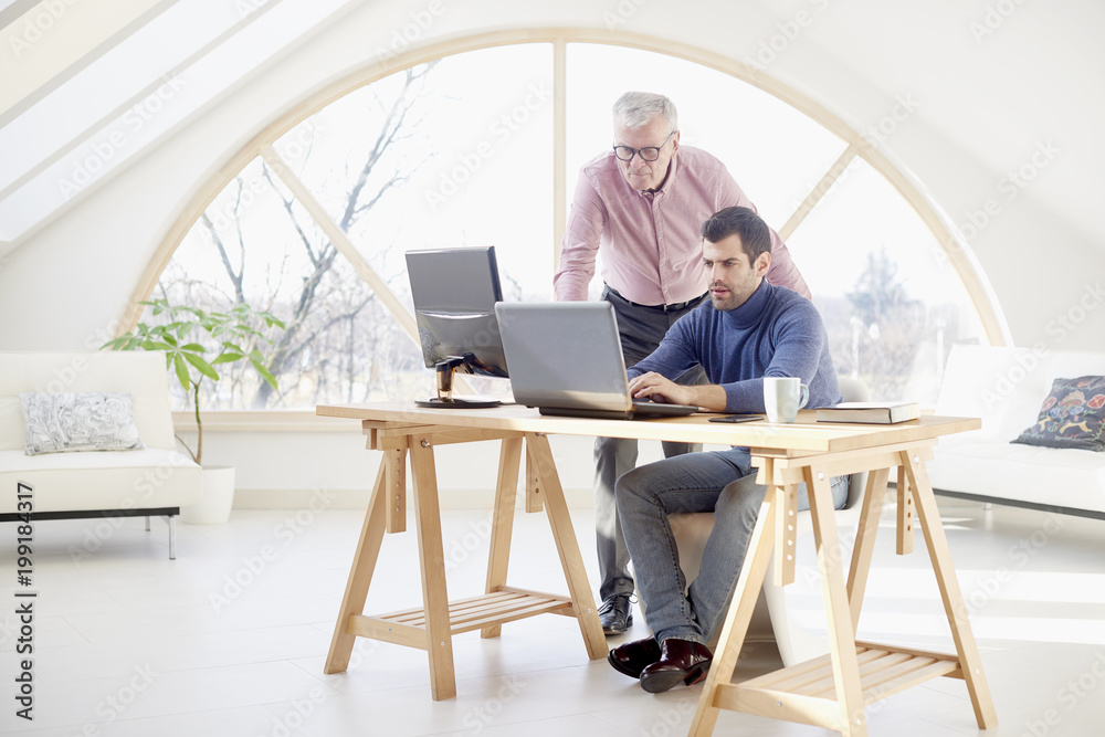 Senior businessman giving adice to her young colleague. Sales assistant sitting in front of laptop and consulting with senior manager while working together on new project. Teamwork at the office. Senior businessman giving adice to her young colleague. Sales assistant sitting in front of laptop and consulting with senior manager while working together on new project. Teamwork at the office.