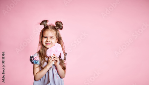 happy little girl in a pink dress, with long brunette hair, on a pink background. Beautiful sweet moments of a little princess, pretty friendly child, having fun looking at the camera