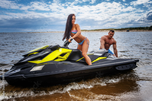 Attractive couple of a sexy girl and shirtless muscular male have fun with a jet ski on a seacoast.