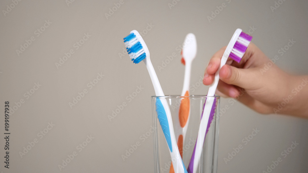 Small childs hand reaches for toothbrush in glass, going to brush teeth, hygiene Small childs hand reaches for toothbrush in glass, going to brush teeth, hygiene