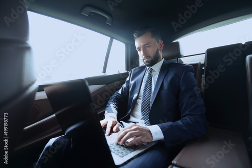 businessman sitting in the back-seat of a car, using his laptop