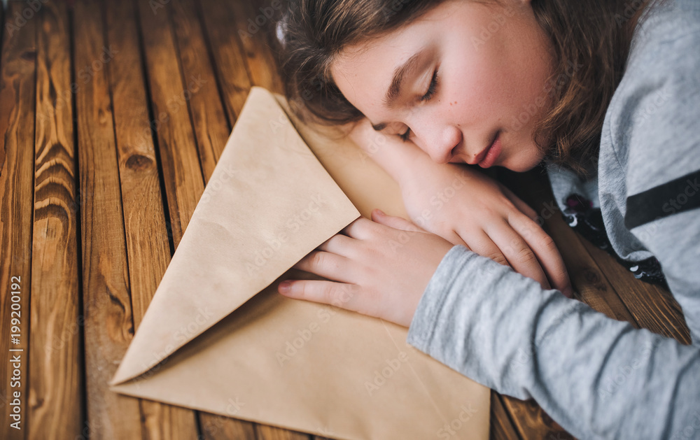Φωτογραφία The little girl tiredly put her head on the table next to a large brown envelope